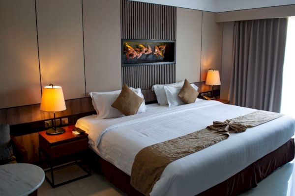 A cozy hotel room with a king-sized bed, soft lighting, decorative pillows, and a wall-mounted art piece above the headboard.