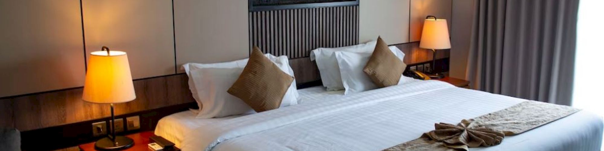 A cozy hotel room features a large bed with pillows, warm lighting, and modern decor.