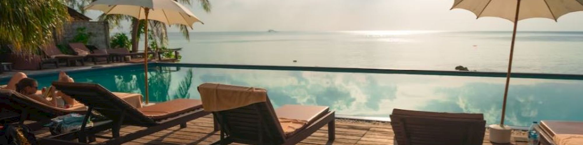 A serene poolside scene with lounge chairs, umbrellas, and a stunning ocean view under a partly cloudy sky.