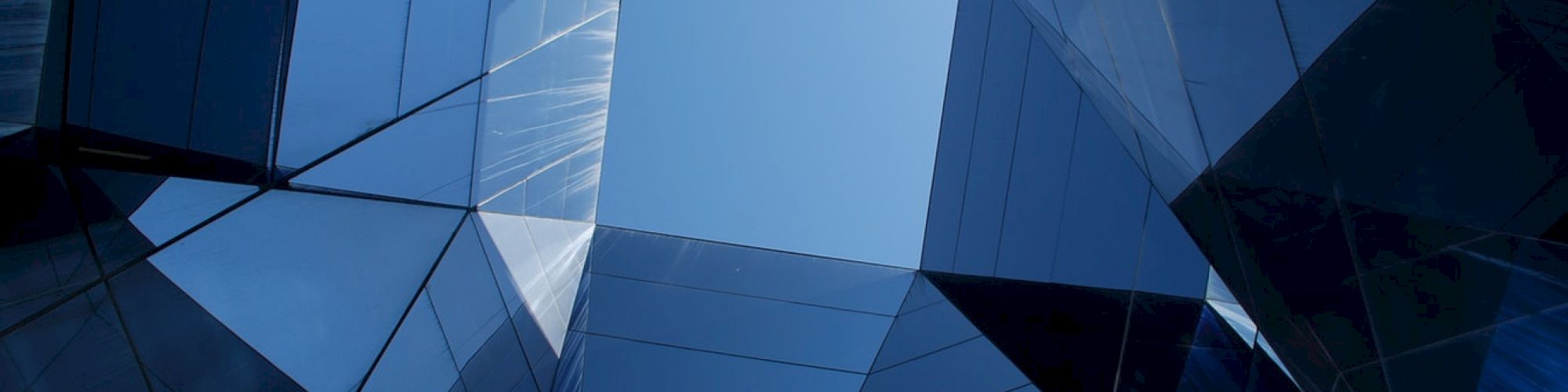 Geometric glass structures form a dynamic pattern, reflecting the sky in vibrant shades of blue.