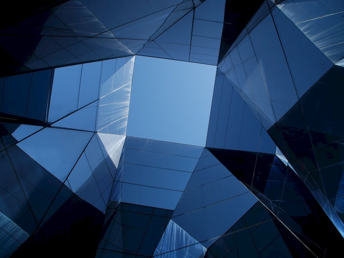 Geometric architectural structure with reflective glass surfaces creating a pattern and open sky visible at the center.