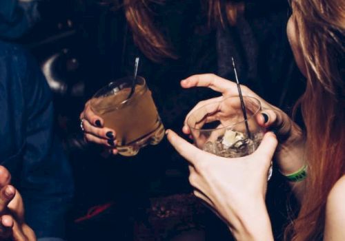 People are socializing and holding drinks in a dimly lit setting, appearing to enjoy a lively conversation.