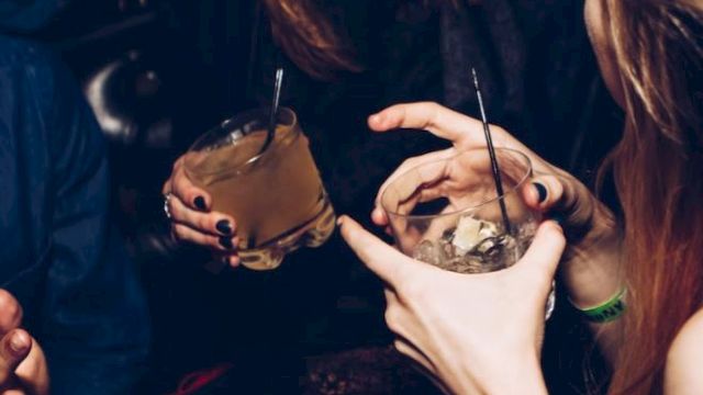 People are socializing and holding drinks in a dimly lit setting, appearing to enjoy a lively conversation.