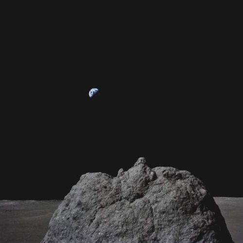 A rocky lunar surface beneath a dark sky, with Earth visible in the distance.