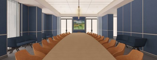 A modern conference room with a long table, orange chairs, blue paneling, a central screen, and ceiling lights.