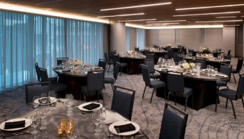 The image shows a banquet hall with round tables set for dining, featuring elegant table settings and dim, ambient lighting.