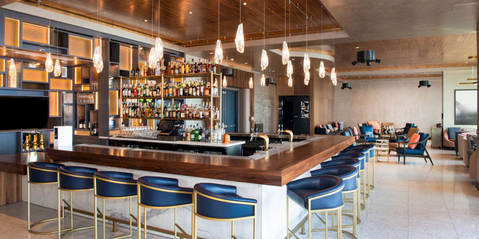 A modern bar with a large selection of bottles, hanging lights, and stylish seating, set in a spacious and elegant interior.