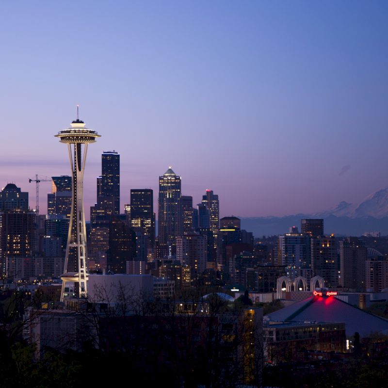 Seattle skyline at dusk featuring the Space Needle, downtown skyscrapers, and Mount Rainier in the background under a purple sky.