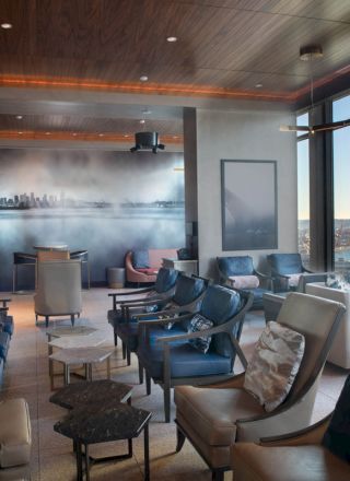 A modern lounge with leather chairs, a cityscape mural, large windows with a waterfront view, and ambient lighting.
