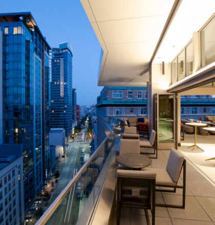 A modern cityscape view from a balcony at dusk, featuring tall glass buildings and a stylish outdoor seating area.