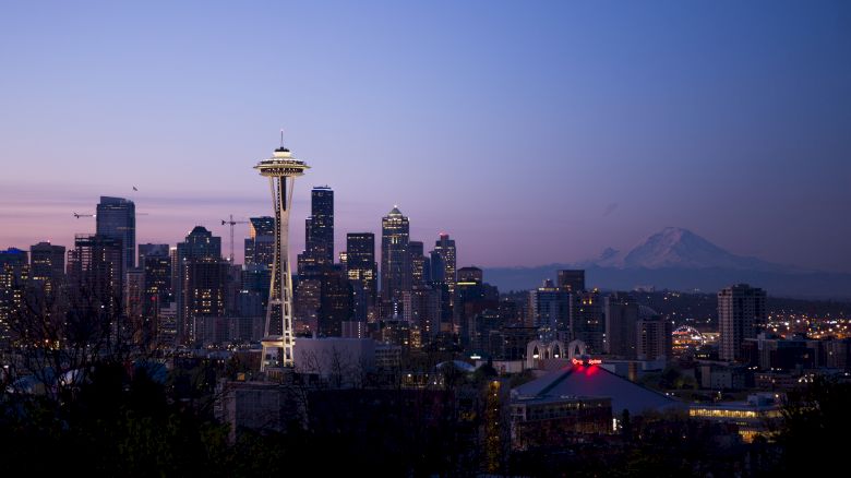 The image shows a city skyline at dusk with the Space Needle and Mount Rainier in the background, likely depicting Seattle.