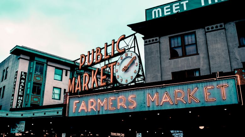 The image shows a neon sign for a "Public Market" and "Farmers Market," with a building and neon lights, suggesting a bustling location.